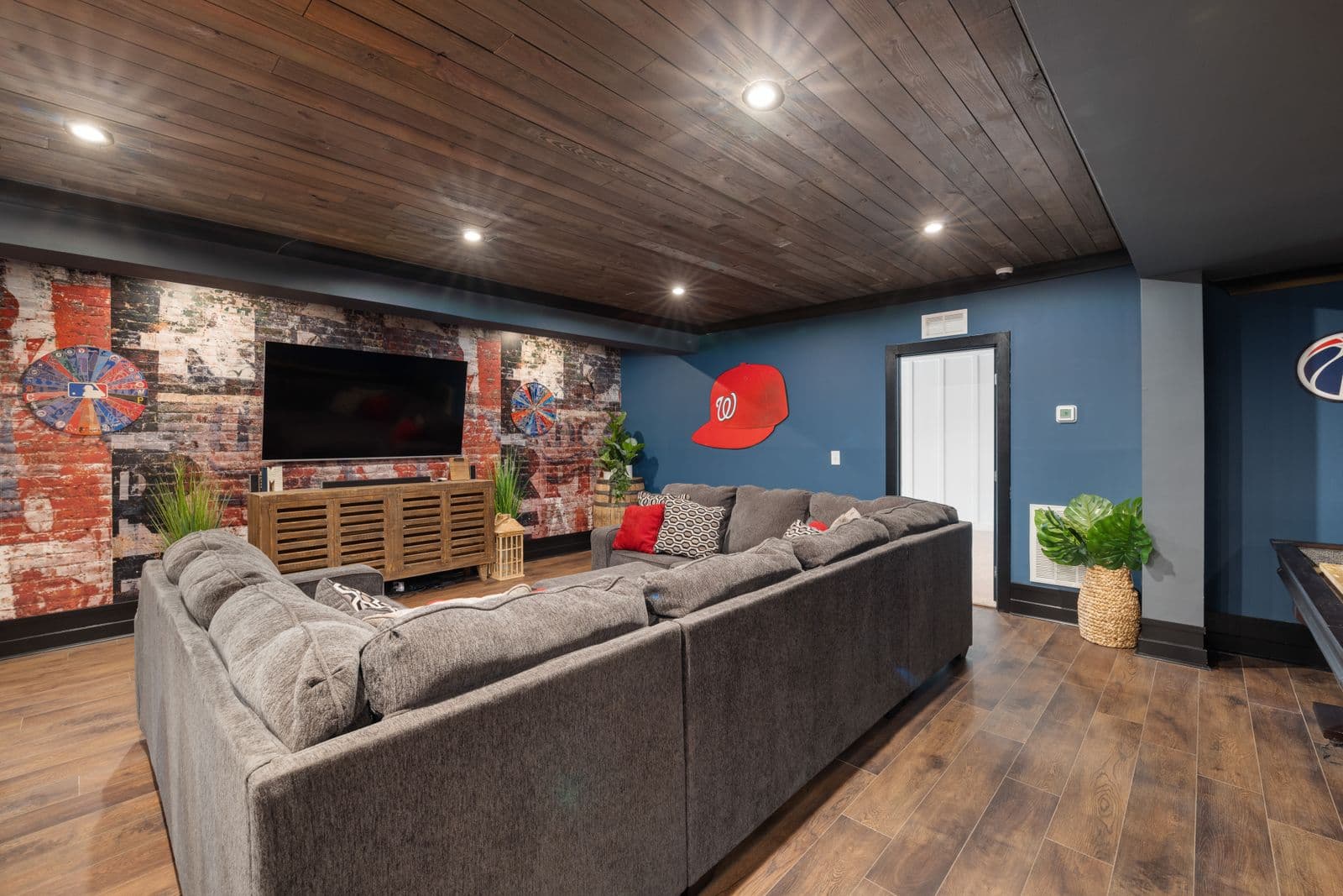 A finished basement family room with a sectional, media area, and warm wood ceiling