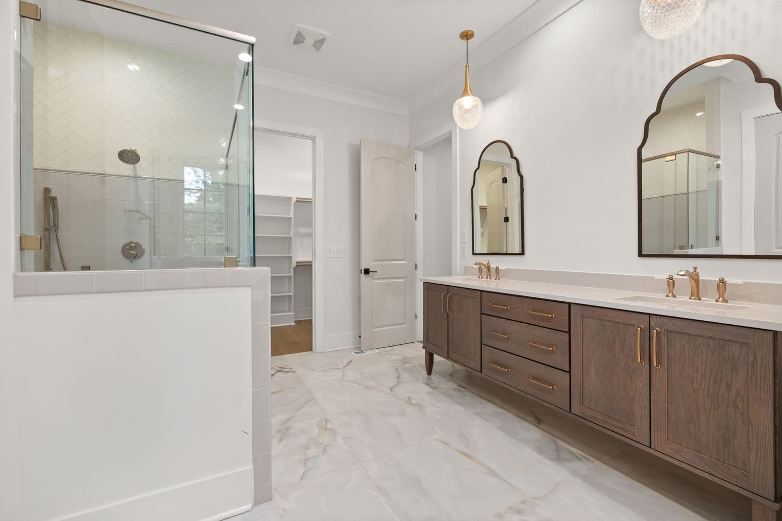A remodeled bathroom with a double vanity, modern lighting, and a glass shower